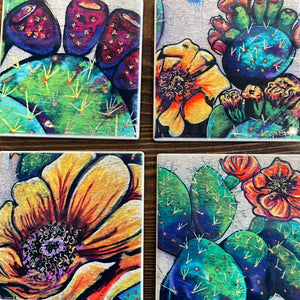 Four colorful ceramic tiles with floral and cactus designs on a wooden surface.